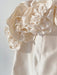 A close-up of the Rosie Dress by Noémiah shows a silk taffeta mini dress adorned with large, intricately crafted fabric flowers. The rose-embellished neckline adds a delicate and elegant touch to the dress, with petals that have a soft, textured appearance while the softly blurred background enhances the details.