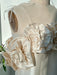 A close-up of the Rosie Dress by Noémiah on a mannequin showcases large, textured fabric flowers crafted from shiny, cream-colored silk taffeta. This mini dress features slim shoulder straps and is ideal for a wedding gown. It is displayed in natural light, casting gentle shadows over its rose-embellished neckline.