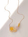 The Samuel Necklace by Noémiah features a delicate and tarnish-resistant thin gold chain, embodying minimalist design with its artful arrangement of several beads: a translucent yellow sphere, a yellow rectangular bead, and a gold square. Displayed elegantly on a light surface, it casts soft shadows that enhance its sophisticated charm.