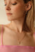 A person with long hair is wearing a pink top and Noémiah's Scarlett Earrings, along with an organic-shaped hoop necklace featuring a small pendant. The photo captures their profile as they look downward, beautifully highlighting the jewelry under soft lighting.