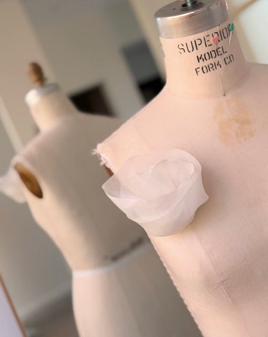 A white dress form with “SUPERIOR MODEL FORM CO” on the neck displays the Noémiah Silk Belt pinned to the chest. Another dress form appears in soft focus in the background, near a mirror.