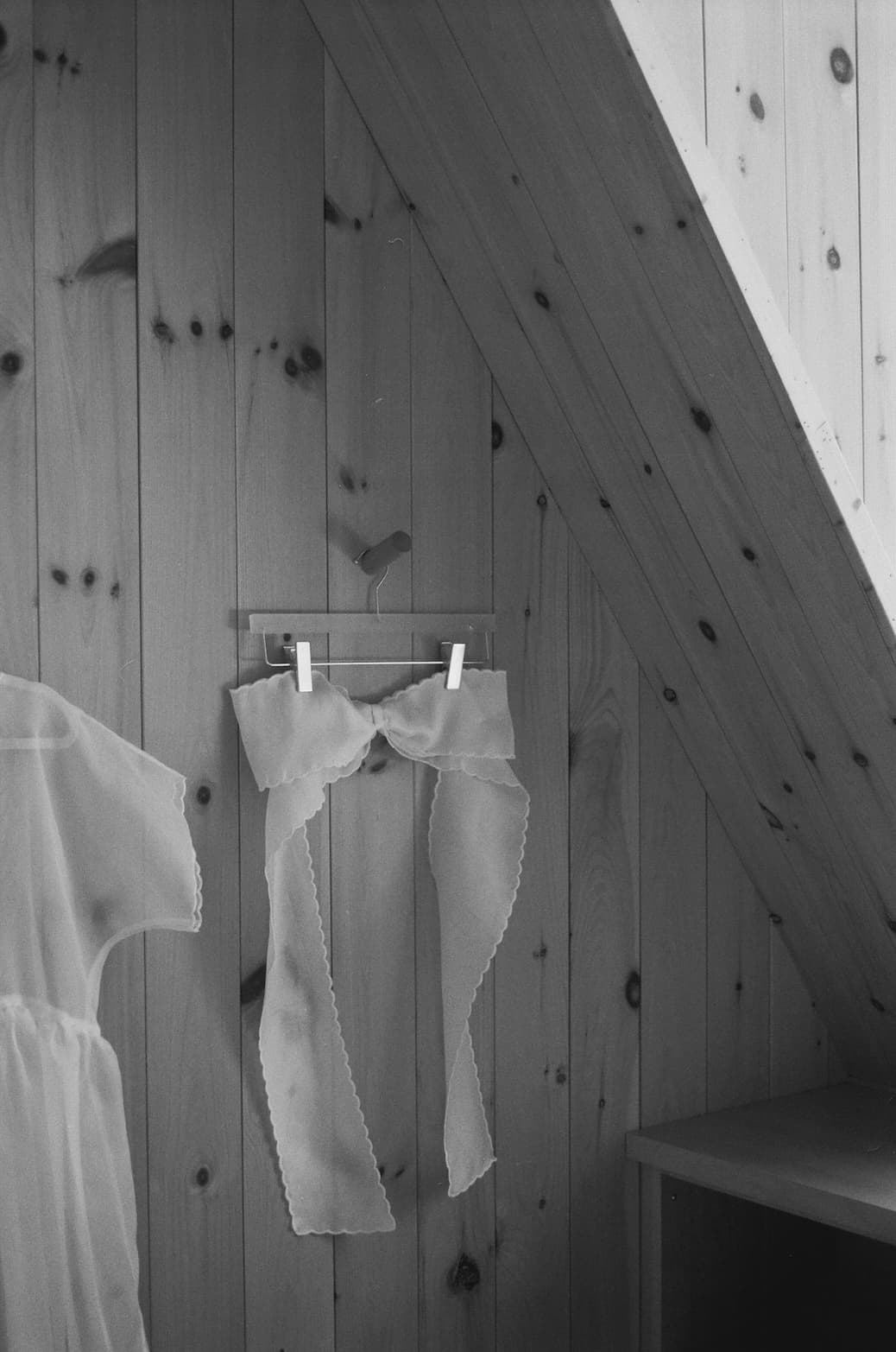 Silk bow by Noémiah hanging on a wooden wall, showcasing delicate fabric and scalloped edges in a rustic setting.