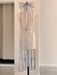 A dress form stands against a white wall, adorned with a Noémiah Silk Ribbon tied into a large bow at the top. The ribbon's long tails drape down the back of the mannequin, showcasing embroidered edges. The floor is concrete.