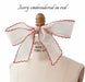 A Noémiah Silk Ribbon in ivory with scalloped edges is embroidered in red and styled as a large bow on a dress form. Text above reads: Ivory embroidered in red.