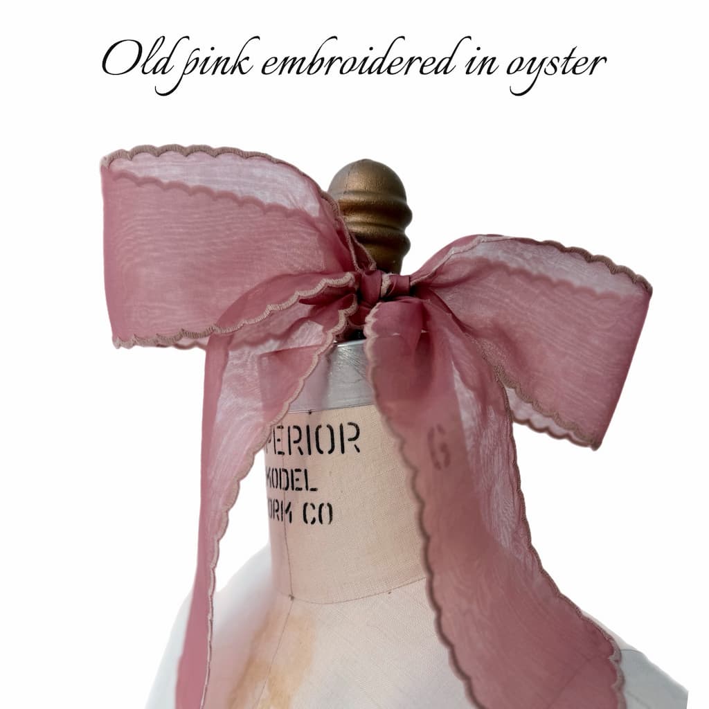 A vintage dress form features Noémiah’s Silk Ribbon — Classic in large, sheer old pink organza with scalloped edges, tied at the neck. Above, elegant script reads “Old pink embroidered in oyster.”.