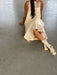 A person sits on the floor in a sleeveless white dress made of organic cotton, paired with Noémiah's Socks — Flowers Hand Dyed Pattern in white with black spots. Their long hair drapes down as they lean back, supported by one arm, with only their torso and legs visible.