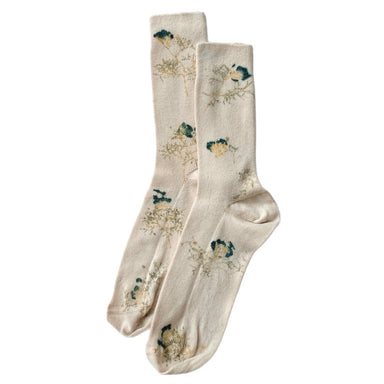 The Socks — Flowers Hand Dyed Pattern by Noémiah showcase a cream-colored design made from organic cotton, featuring a floral pattern accentuated with blue and green elements. This limited edition piece boasts a delicate and natural aesthetic, offering a subtle decorative touch to the fabric.