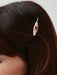 A close-up of brown hair styled with Three Hair Clips by Noémiah, featuring handmade porcelain accents—a white leaf and a red rose. The accessory is in focus, while the person’s face appears partially visible.