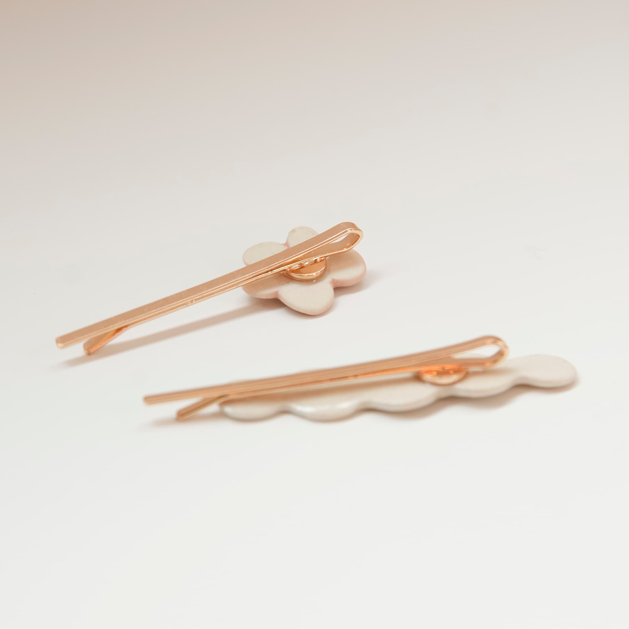 Noémiah’s Three Hair Clips set features handmade 22-karat gold porcelain clips with white ceramic designs, including a flower shape and a wavy-edged piece, displayed on a white surface.