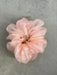 A close-up of a pink, sheer tulle scrunchie from the "Three Scrunchies" collection by Noémiah is displayed on a gray textured background. Crafted from 100% silk organza, this delicate accessory boasts a puffy appearance reminiscent of layers of flowers and resembles Tulip Dress scraps.