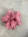 A pink, sheer fabric scrunchie from Noémiah's "Three Scrunchies" collection, made from tulip dress scraps, rests elegantly on a gray textured surface.