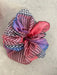 A vibrant, see-through scrunchie made from Tulip Dress remnants by Noémiah blends pink, blue, and checkered designs on a light gray background. This is part of their Three Scrunchies collection.