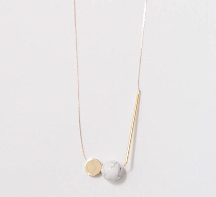 The Urso Necklace by noemiah is a minimalist piece featuring tarnish-resistant plating and a delicate chain adorned with three unique pendants: a gold disc, a marble-like sphere, and a gold cylindrical bar, embodying modern elegance.