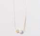 The Urso Necklace by noemiah is a minimalist piece featuring tarnish-resistant plating and a delicate chain adorned with three unique pendants: a gold disc, a marble-like sphere, and a gold cylindrical bar, embodying modern elegance.