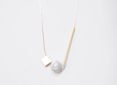 The Urso Necklace by noemiah is a minimalist piece featuring tarnish-resistant plating, a thin gold chain, and a geometric pendant showcasing a gold square, white marble-like sphere, and gold rod.