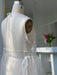 A dress form displays a sheer, white Noémiah Vivi Dress featuring sophisticated cutout details and delicate ties in a brightly lit room. In the background, there is a sleek white counter adorned with a vase filled with vibrant flowers.