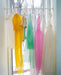 Colorful sheer Noémiah dresses and garments hanging on a white window rod.