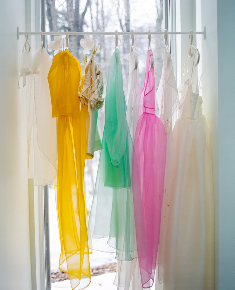 Colorful sheer Noémiah dresses and garments hanging on a white window rod.