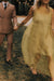 A person in a sheer yellow Noémiah Vivi dress holds hands with a person in a tan double-breasted suit while walking outdoors.